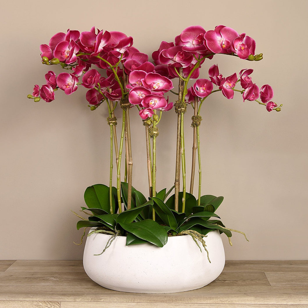 Artificial flower arrangement with pink orchids in white planter